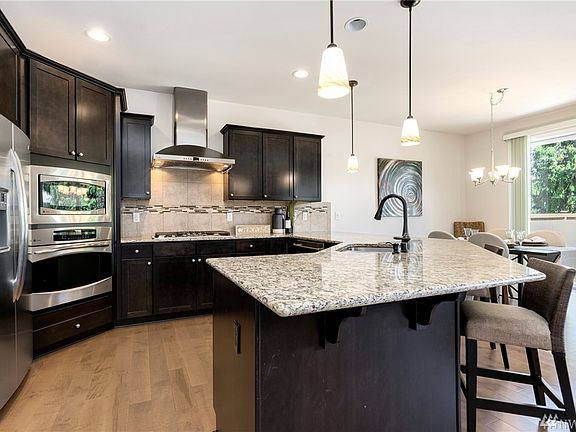 Chef's kitchen with rich, dark cabinetry, full tile backsplash, stainless-steel appliances & gas cooking.