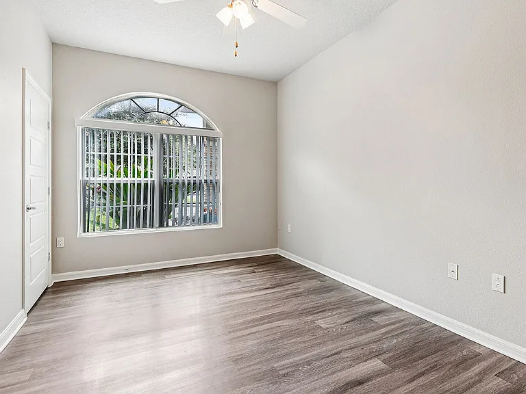 Bright and inviting bedroom featuring elegant hardwood floors, large arched window, and soothing neutral walls.