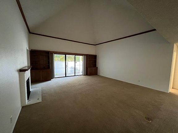 large living room features a working gas fireplace, cathedral ceiling and access out to the patio