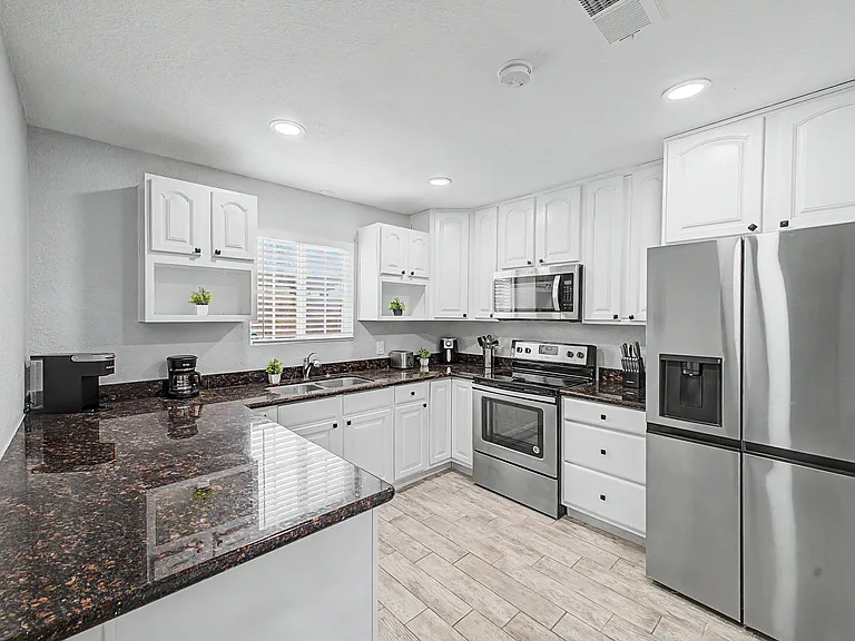 Spacious U-shaped kitchen with ample white cabinetry, granite-look counters, and stainless steel appliances plus a windowed s