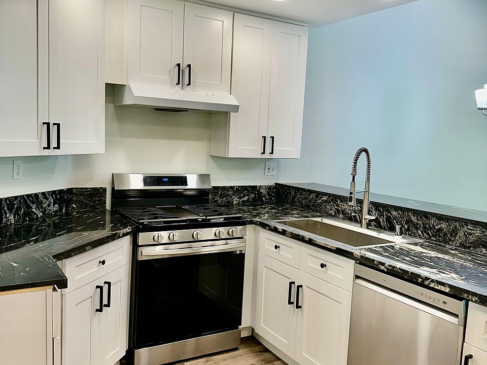 Gorgeously renovated kitchen with high-end quartz countertops and white shaker cabinets and stainless sink and appliances.