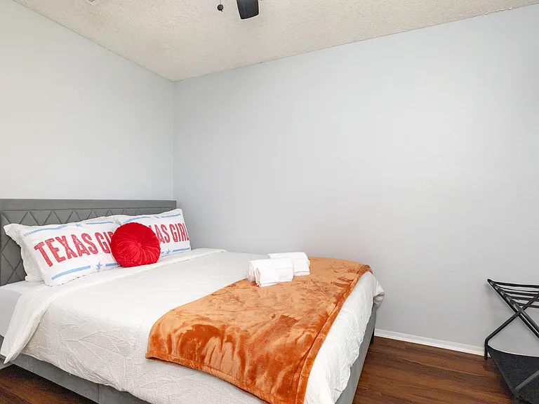 This inviting second bedroom features a queen bed with playful "Texas Girl" pillows and a warm orange throw.
This bright and airy guest room offers a comfortable queen bed and a convenient luggage rack for travelers.