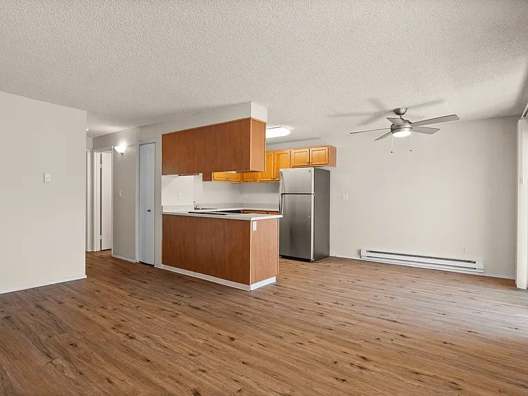Modern open-plan living area featuring elegant wooden flooring, a stylish kitchen with a stainless steel refrigerator, and a ceiling fan for enhanced comfort. Modern open-plan living area featuring elegant wooden flooring, a stylish kitchen with a stainle