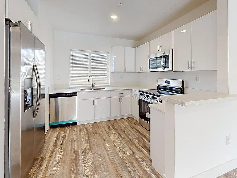 Bright, modern kitchen with sleek stainless steel appliances, stylish wooden flooring, and ample white cabinetry.
