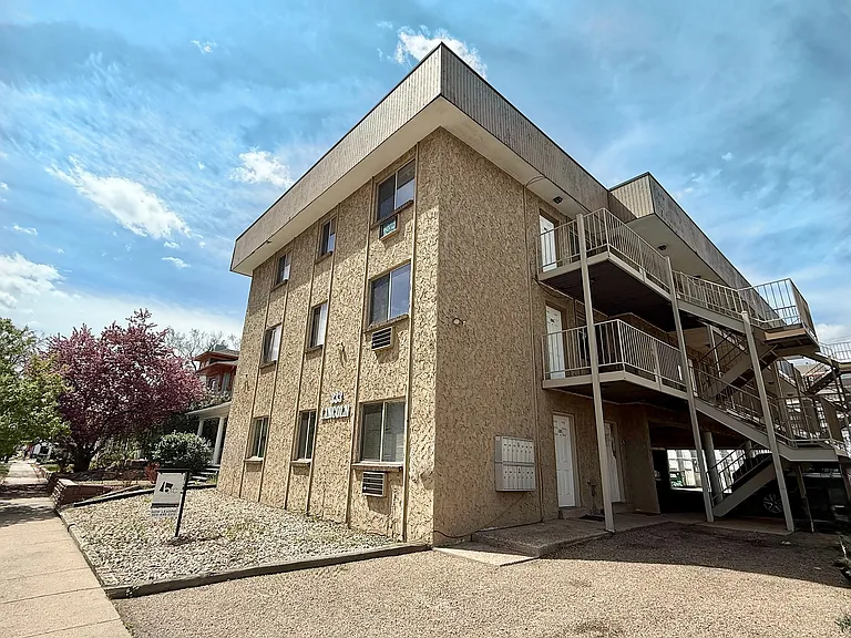 Charming apartment building with textured exterior, featuring outdoor staircases and scenic landscaping under a bright sky.