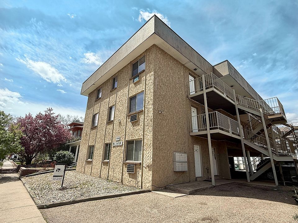 Charming apartment building with textured exterior, featuring outdoor staircases and scenic landscaping under a bright sky.