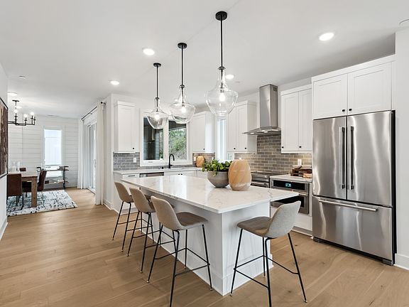 A modern, open-concept kitchen with a large island, stainless steel appliances, and pendant lighting