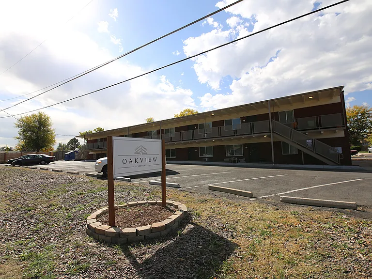 Inviting Oakview Apartments exterior with ample parking, surrounded by serene green spaces under a bright blue sky.