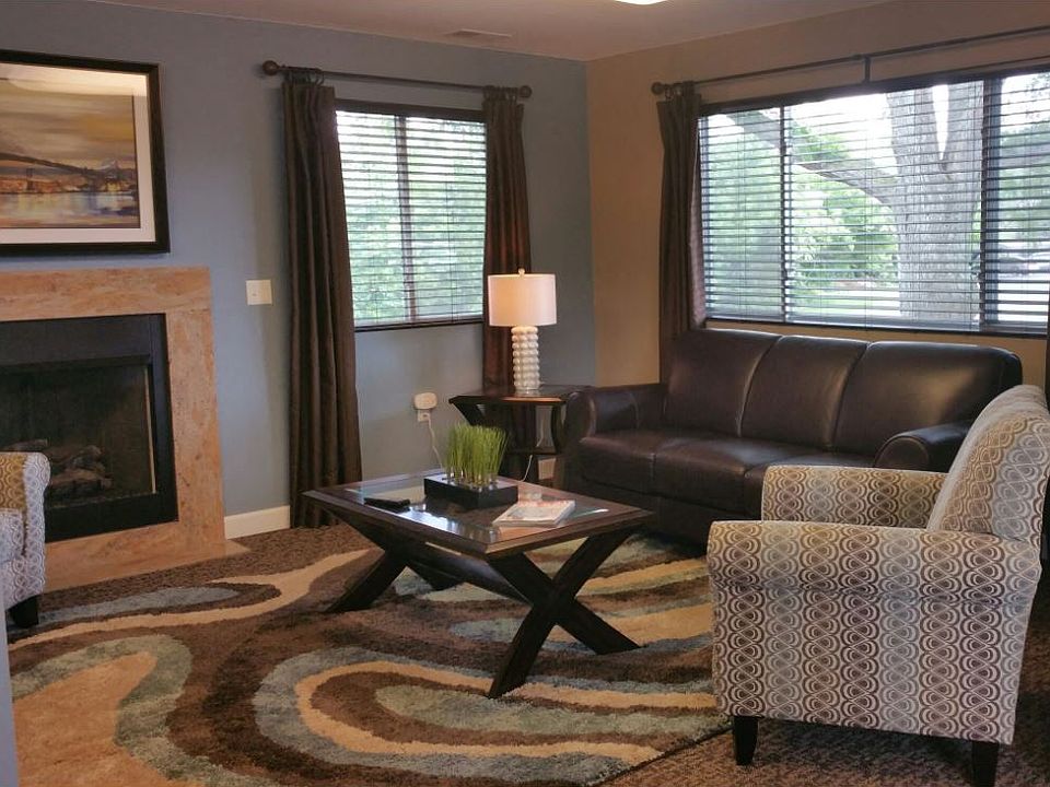 Leasing office sitting area with a brown leather couch under a large window, a stripped patterened sitting chair, a glass and wood coffee table and a fireplace.
