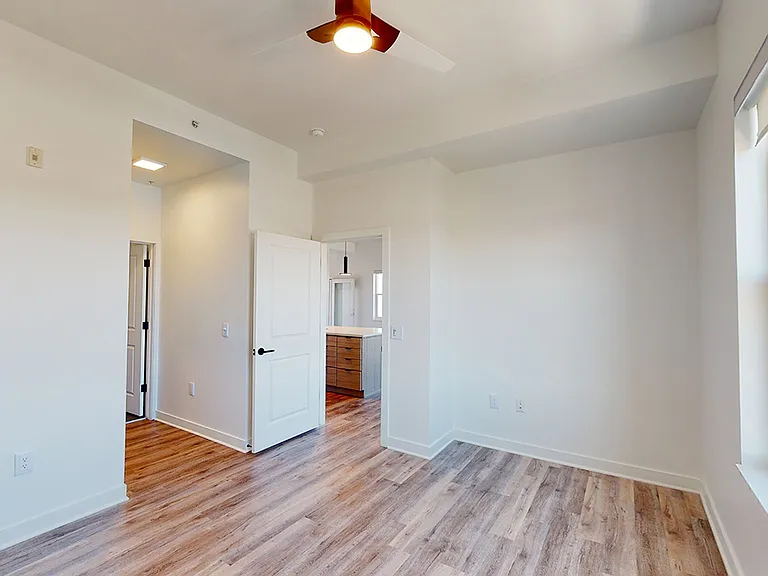 Spacious apartment bedroom with large closet, attached bathroom and wood-style flooring.