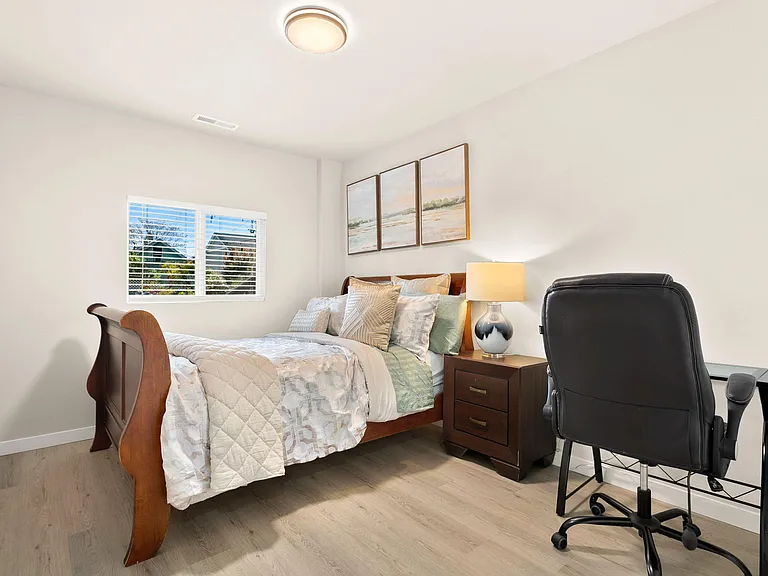 Furnished bedroom with a wood sleigh bed, nightstand lighting, window with blinds, and a dedicated desk workspace.