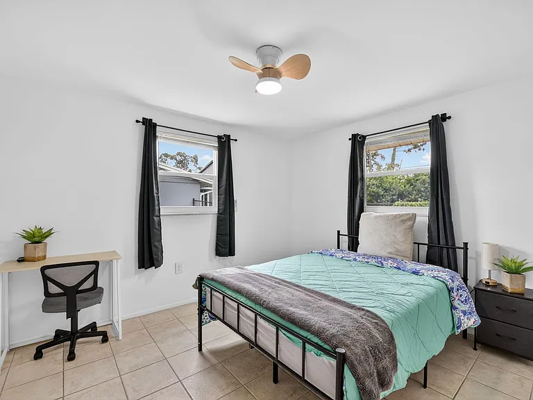Furnished bedroom with two windows, ceiling fan, nightstand, and a dedicated desk space for work or study.