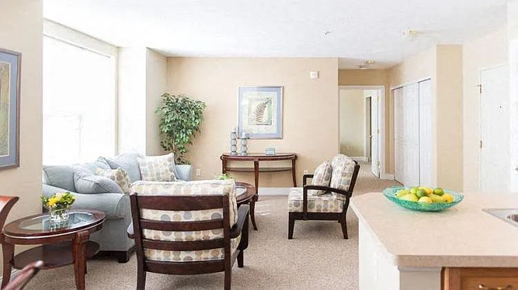 Spacious living room area in great room of 2-bedroom ranch style apartment with large, bright windows and hallway to 2nd bedroom in the background