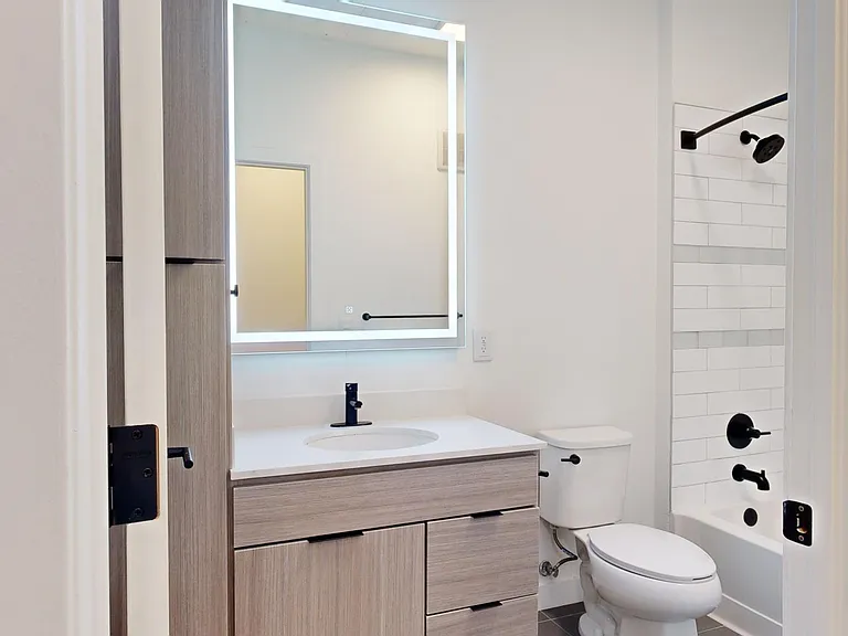 Apartment bathroom with wood-style flooring and LED vanity mirror.