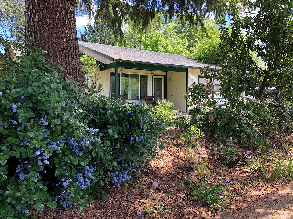 Front of house, showing covered front porch and garage access to right. Lot of native plants!