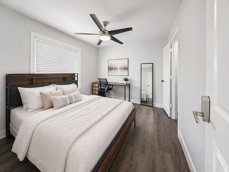 Spacious bedroom with a full bed, ceiling fan, and wood-look floors, plus a dedicated desk area and closet access.