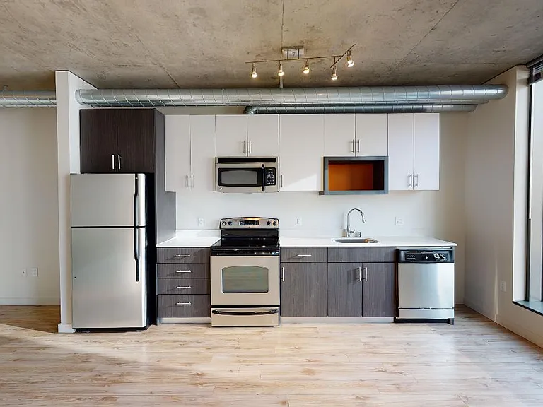 Apartment kitchen with stainless steel appliances, quartz countertops and wood-style flooring.