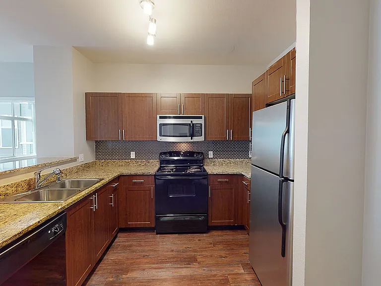 Apartment kitchen with granite countertops and wood-style flooring.