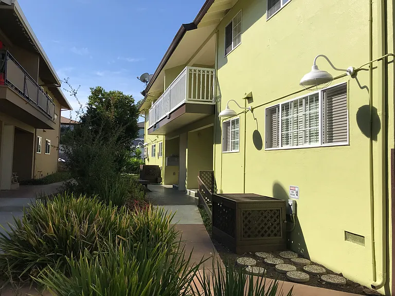 Cozy 600 square foot apartment with a front porch entry that opens to a landscaped common area and concrete walkway with wooden benches.