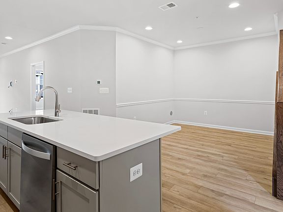 Open kitchen with light toned wood floors, gray island and white countertops that opens to formal di