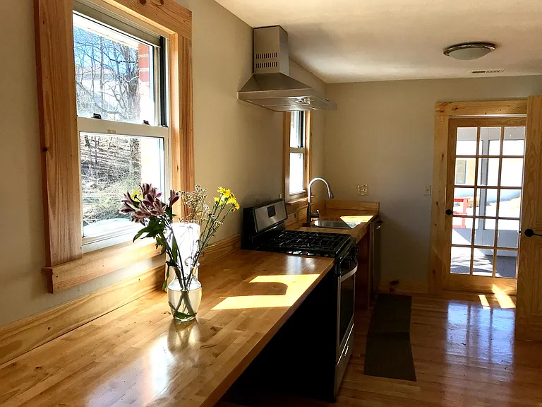 Kitchen. Butcher block counters, gas stove with hooded vent to exterior. Door to sun room on far side. Flooring is red oak.