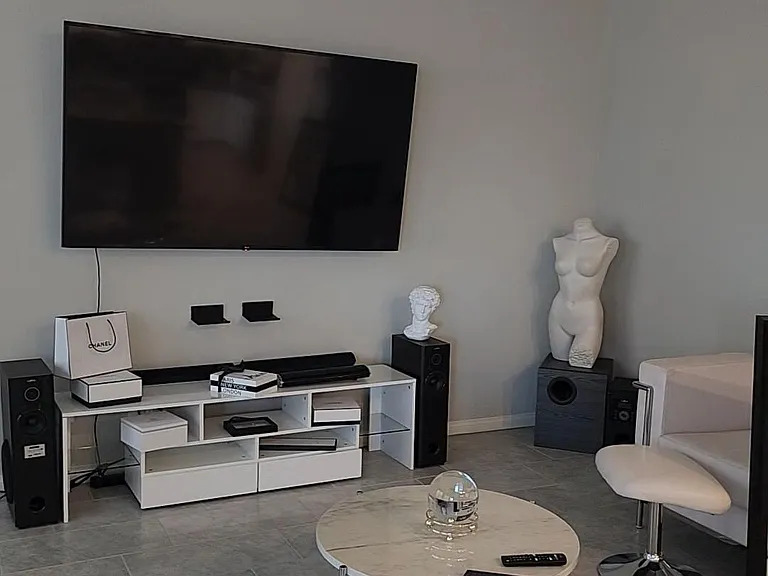 Open living area with tile flooring, ceiling fan, and a wall-mounted TV with media console and lounge seating.
