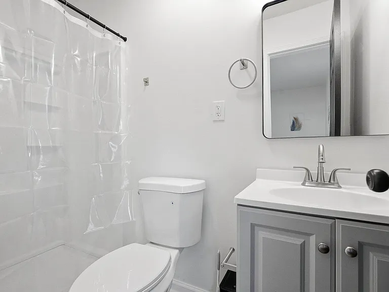 Compact full bathroom with tub/shower combo, vanity with storage, and wall mirror for daily routines.