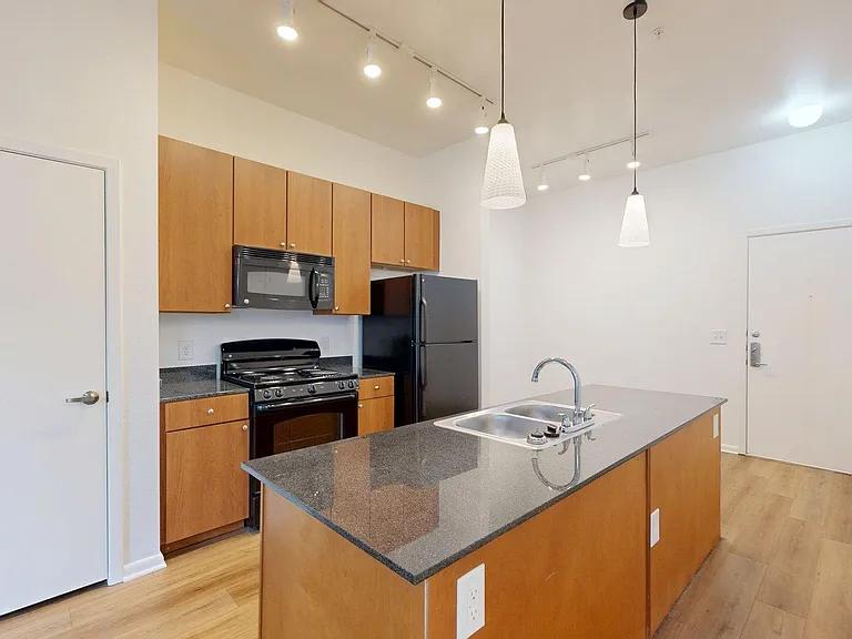Apartment kitchen with dark counters and wood style floors.