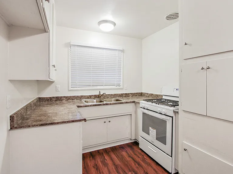 Kitchen with granite countertops, white gas range, white cabinets, and wood style flooring