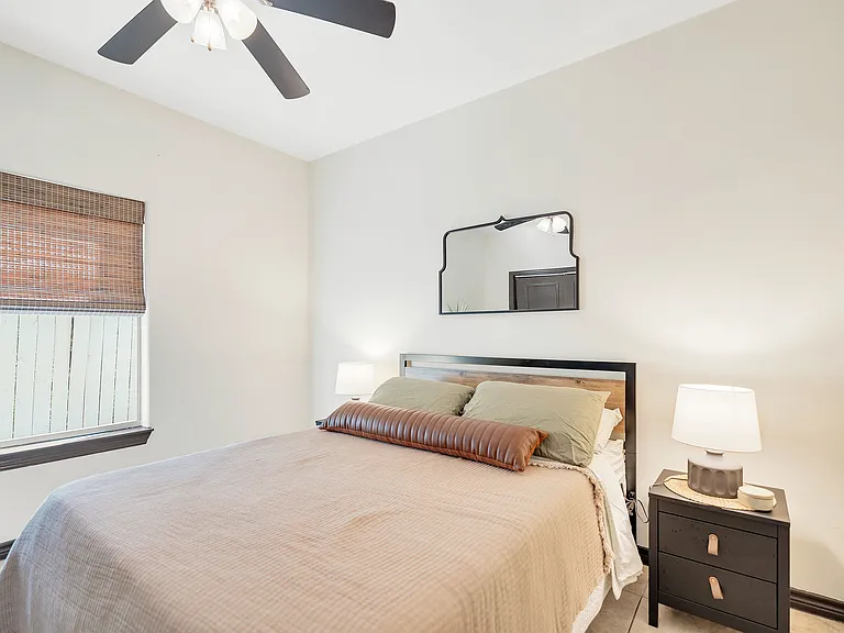 Interior of a La Joya Apartments bedroom with a bed, nightstand, and ceiling fan, showcasing a welcoming atmosphere..