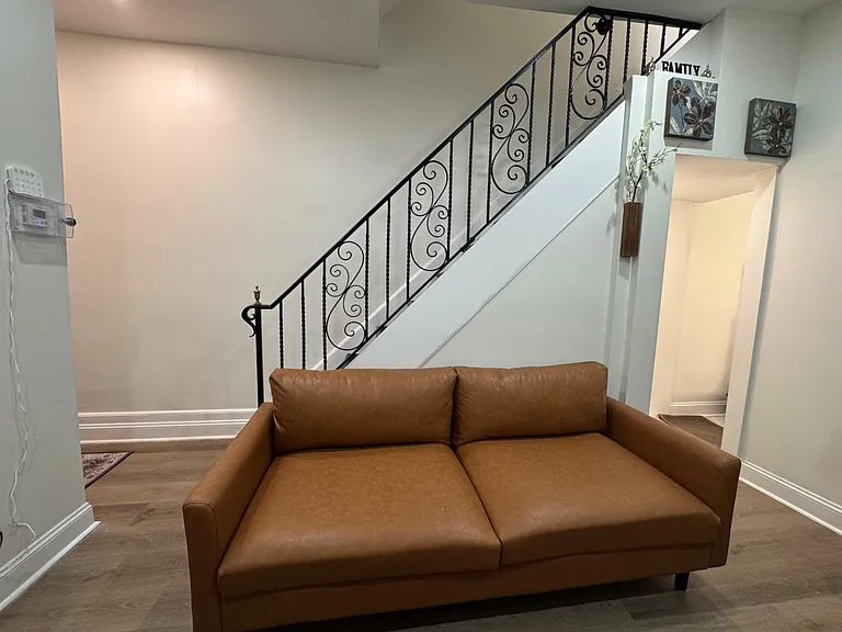 Shared living area with leather sofa seating, durable flooring, and an open stairwell layout connecting to nearby rooms.
