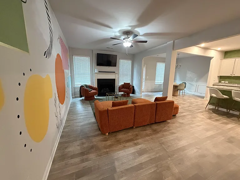 Open-concept living area with ceiling fan, fireplace, and wall-mounted TV, flowing into a breakfast bar and dining nook.
