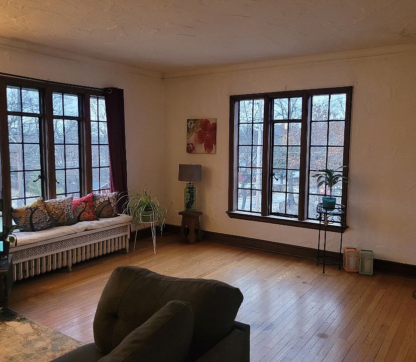 Spacious living room with large original windows and hardwood floors.