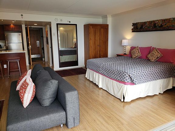 View of the king sized bed, armoire, sofa sleeper, kitchen area.