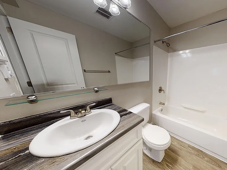 The bathroom in our Hampshire studio floor plan features a large mirror, wood-style flooring, and upgraded countertops.