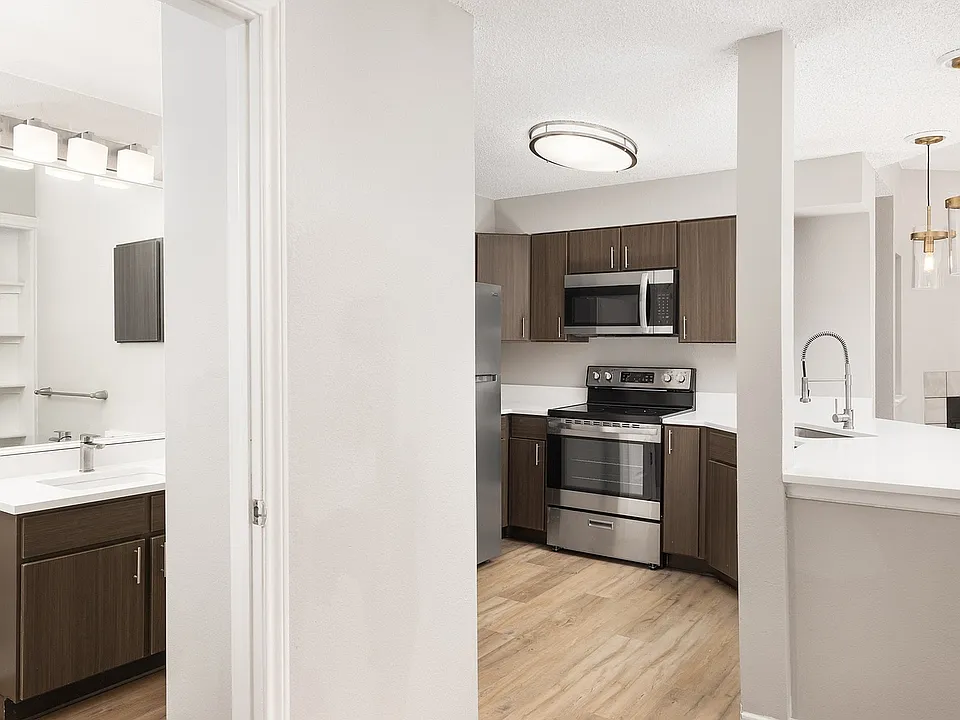 Modern apartment kitchen with elegant white countertops, stainless steel appliances, and warm wood flooring.
