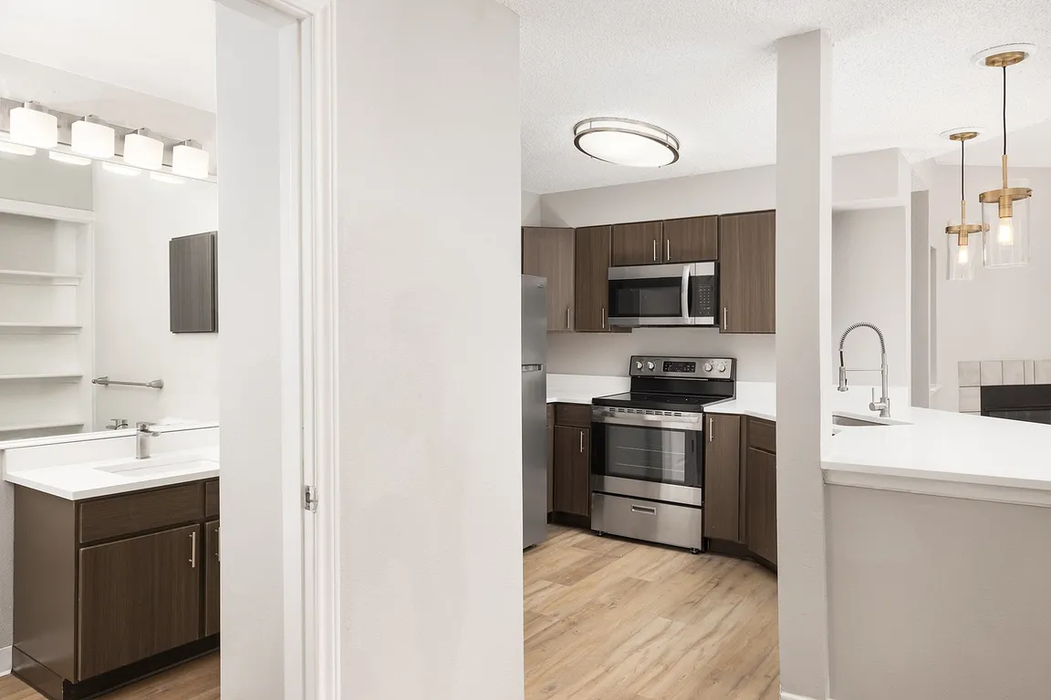 Modern apartment kitchen with elegant white countertops, stainless steel appliances, and warm wood flooring.