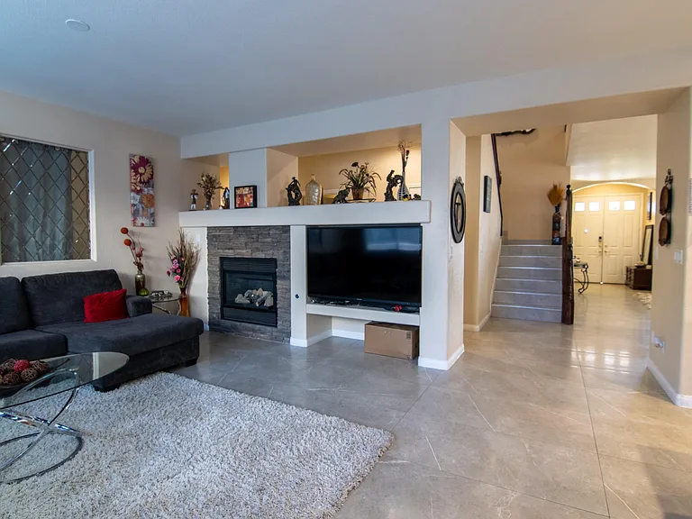 Open living area with tile flooring, a built-in media nook, and a stone-accent fireplace, flowing into the entry hall.