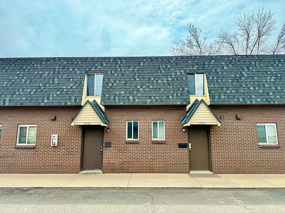 Charming brick duplex with modern roofing, featuring dual entryways and lush surroundings.