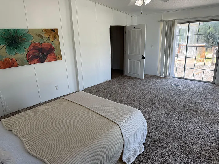 Spacious carpeted bedroom with sliding glass doors to a private patio/deck, plus ceiling fan and ample wall space.