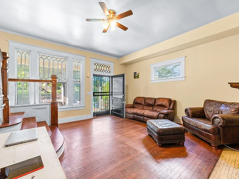 Spacious living area with hardwood floors, large windows, ceiling fan, and seating space near the front entry.