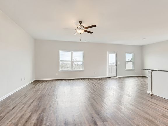 Spacious family room with wood-style flooring throughout, a ceiling fan, and windows.