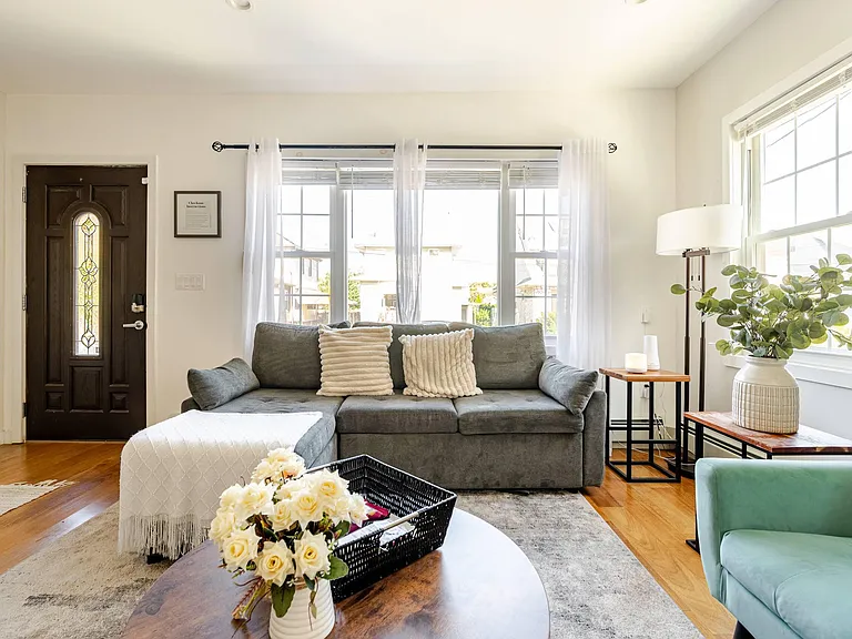 Living room with a sectional, large windows and airy curtains, plus side tables and lamps for comfortable lounging.