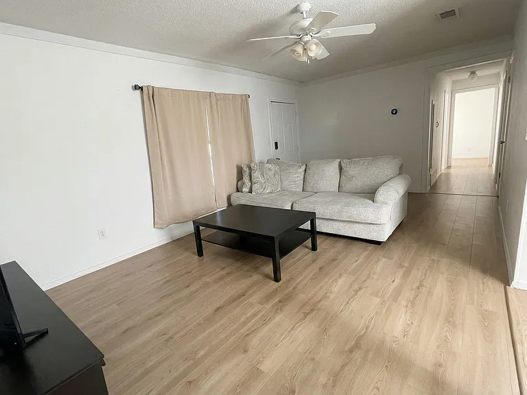 Living area with wood-look flooring, ceiling fan, and comfortable seating with room for a coffee table and TV setup.