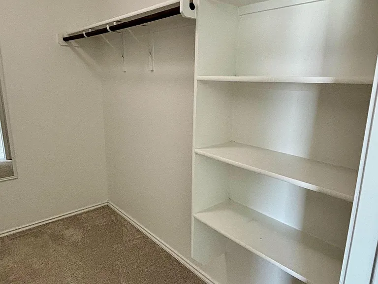 Spacious walk-in closet with built-in shelving and a hanging rod for organized storage of clothes and accessories.