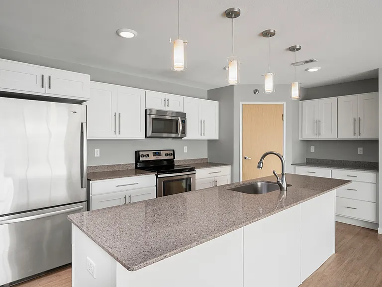 Modern kitchen with sleek stainless steel appliances, white cabinetry, and a large island with granite countertops and pendant lighting. Modern kitchen with sleek stainless steel appliances, white cabinetry, and a large island with granite countertops and