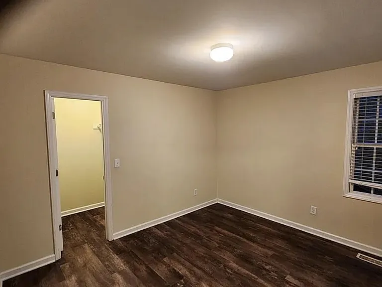 Spacious unfurnished bedroom with wood-style floors, neutral walls, and a window with blinds for natural light.