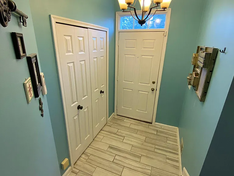 Spacious foyer with tiled floors, double coat closet, and chandelier.
