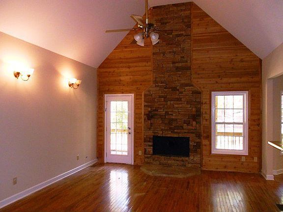 Large great room with wood paneled accent wall, wood stove hearth area, sconces, cathedral ceilings,