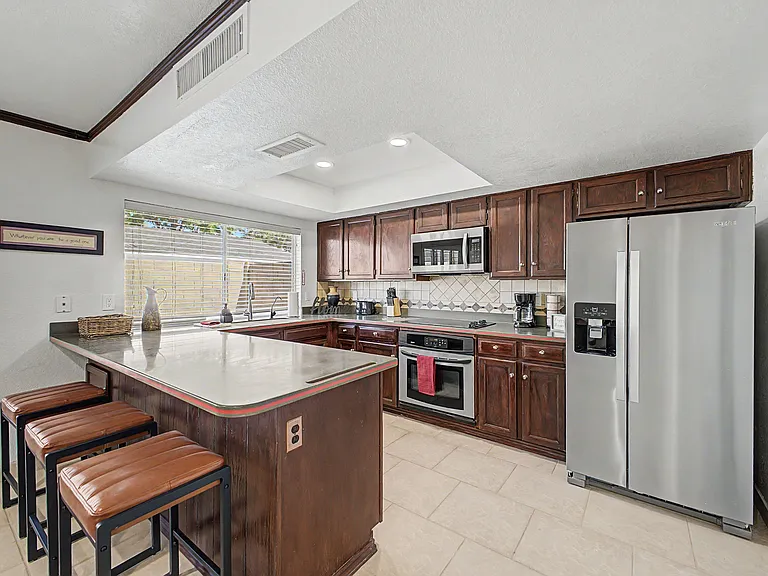 Eat-in kitchen with a large peninsula, ample wood cabinetry, tile backsplash, and stainless steel appliances.